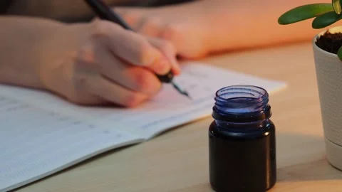 A girl sits at the table and writes with a pen and ink. Stock Footage 229488564