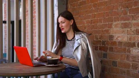 Girl sits at a table in a cafe with mug of coffee and talks video call computer Stock Footage 137563998