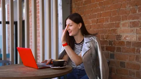 Girl sits at a table in a cafe with mug of coffee and talks video call computer Stock Footage 137564533