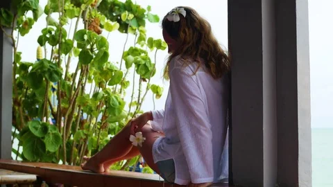 The girl sits on the terrace and looks towards the sea.Holding flowers in his Stock Footage