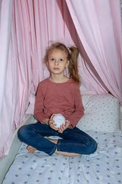 The girl is sitting on the bed and looking at something through the projector Fotos Stock