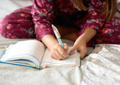 Girl sitting on a bed and writing on a notebook Stock Photos