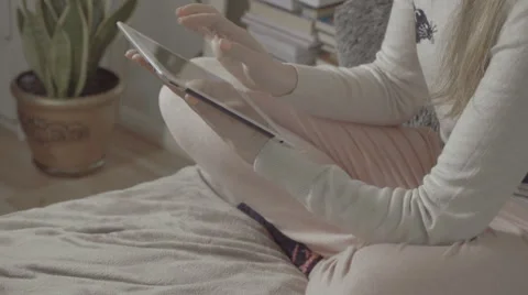 Girl sitting on bed at home using tablet. Stockbeeldmateriaal 61673636