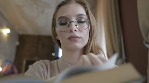 Girl sitting in a cafe at the table with a Cup of coffee and reading a book. Video stock 108590553