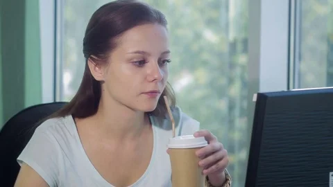 A girl sitting at a computer in a room by the window smiles and drinks coffee Stock Footage 80244413