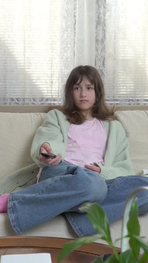 Girl sitting on the couch at home, using the remote control to switch channels Stock Footage 275016397