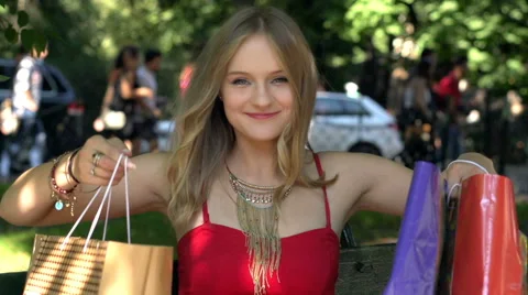 Girl sitting down with shopping bags and smiling to the camera, slow motion shot Stock Footage