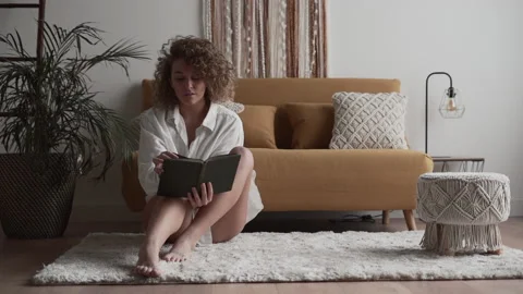 Girl sitting in front of the sofa checking a book Stock Footage 220855099