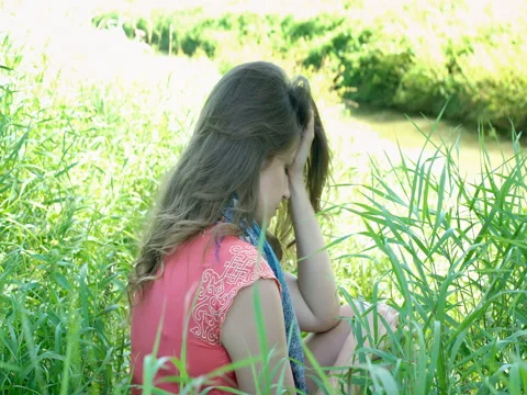 Girl sitting in the grass and looks very sad and lonely, steadycam shot Stock Footage