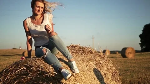 Girl sitting on a haystack during sunset. the guy jumps on a haystack. Stock Footage 61816013
