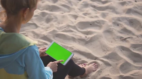 A girl sitting on the sand and using a tablet with chroma key screen. Swiping. Stock Footage 83672219