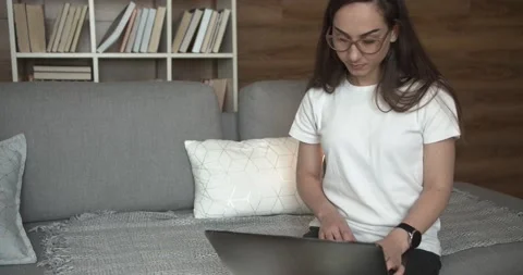 Girl sitting on a sofa types the text on a laptop. Concept of working from home Video stock 132445177