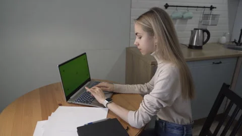 Girl sitting at table in kitchen working on laptop and answering smartwatch call 스톡 동영상 260541320