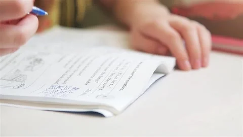 Girl sitting at the table writing in a notebook homework in English Stock Footage 105963435