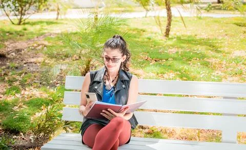 A girl sitting taking notes with a notebook and cell phone, Woman sitting t.. Stock Photos