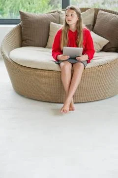Girl sitting in a wicker couch using a digital tablet Stock Photos