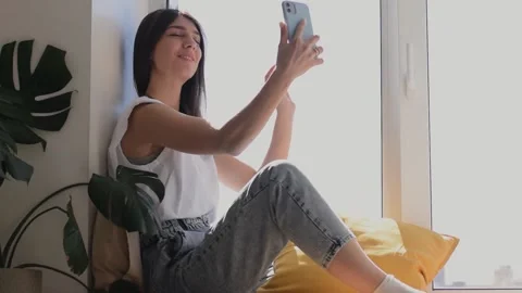 Girl is sitting on the windowsill and taking a video of herself on a smartphone. Stock Footage 152837745