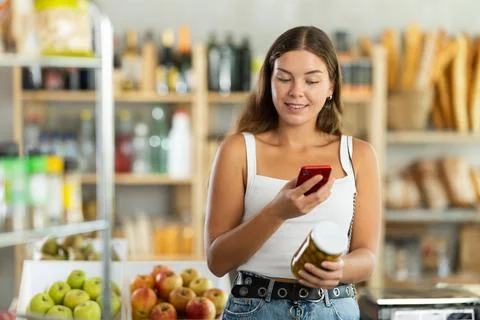 Girl with smartphone scans QR code on a jar of canned olives in the produce Stock Photos