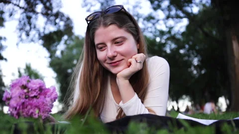 Girl smelling flowers while lying on blanket in green park Stock-Footage 134074604