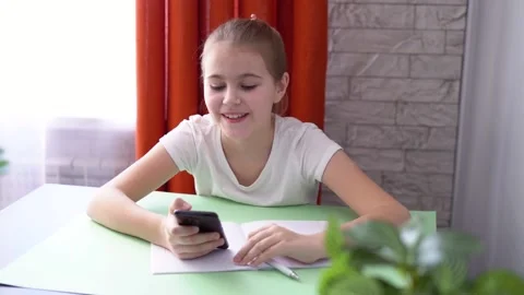 The girl smiles, does her homework and looks at the phone. distance education Stock Footage 176427633