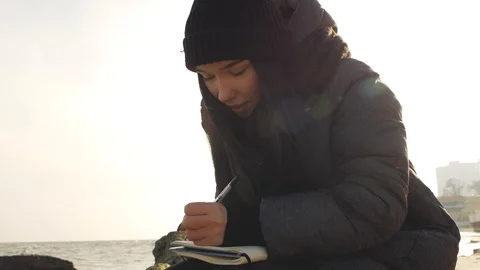 The girl is smiling and preparing to write with a pen in a notebook sitting o Stock Footage 103053046