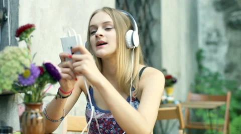 Girl smiling to the camera while listening music and texting on smartphone Stock Footage