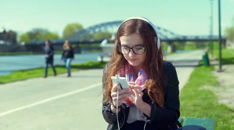Girl smiling to the camera while using smartphone and listening music on headpho Stock-Footage 66521538