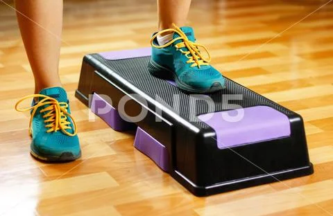 The girl in sneakers is engaged on the step-platform for fitness. Feet on the Stock Photos