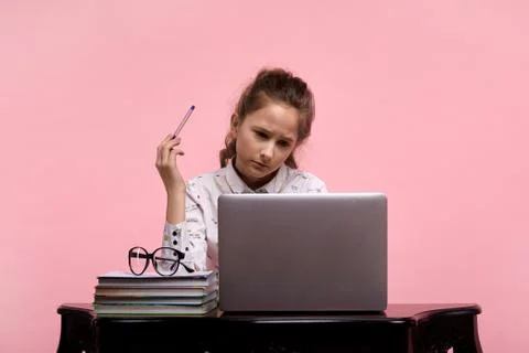 Girl of solves problems in a laptop next to a stack of books. Stock Photos