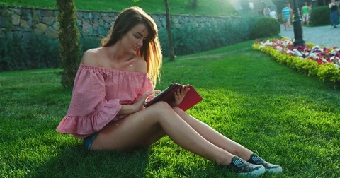 The girl is spending time in the park while sitting on the grass. Girl is Stock Footage 84757726