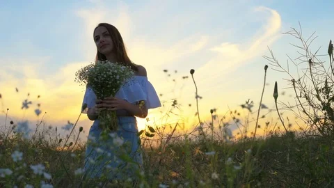 Girl is standing in a field holding a bouquet in her hands. Stock Footage