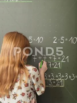 Girl standing in front of blackboard, solving arithmetic problem, rear view Stock Photos