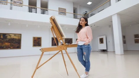 Girl standing in front of blank canvas in art gallery. Stock Footage