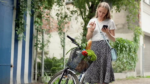 Girl standing with her bicycle and checking shopping in the basket Stock Footage