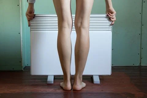 The girl is standing near the heating convector in the middle of the bedroom, Stock Photos