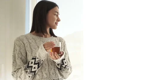 Girl standing thinking by window drinking te Stock Footage 221946939