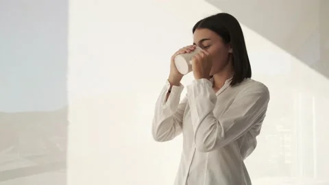 Girl standing thinking by window drinking coffee Stock Footage 221946988