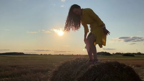 Girl stands carefully up on rolled haystack. Silhouette of girl against sunset 스톡 동영상 163905288