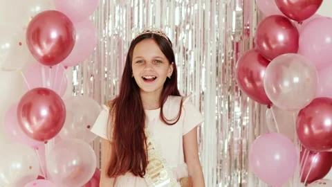A girl stands in front of a backdrop of balloons and shiny decorations, smiling Stock Footage 336460926
