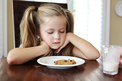 Girl staring at cookie with milk at table Stock Photos