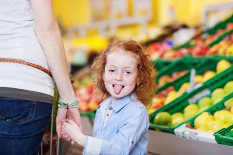 Girl sticking out tongue while holding mother's hand in grocery Stock Photos