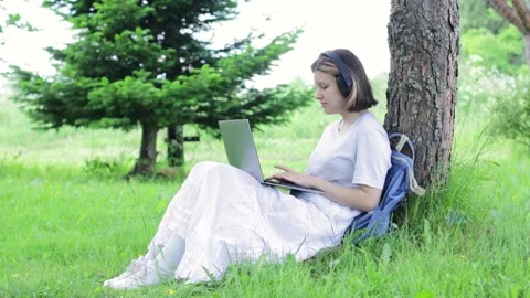 Girl student prints on a laptop while sitting in the park. Teenager performs Stock Footage 157917152