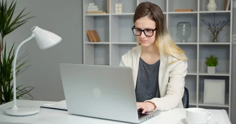 Girl student uses a laptop while sitting in the room. Young woman freelancer Stock Footage 148550829