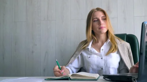 Girl student writes in a notebook a language lesson from the monitor. Distance 스톡 동영상 136592632