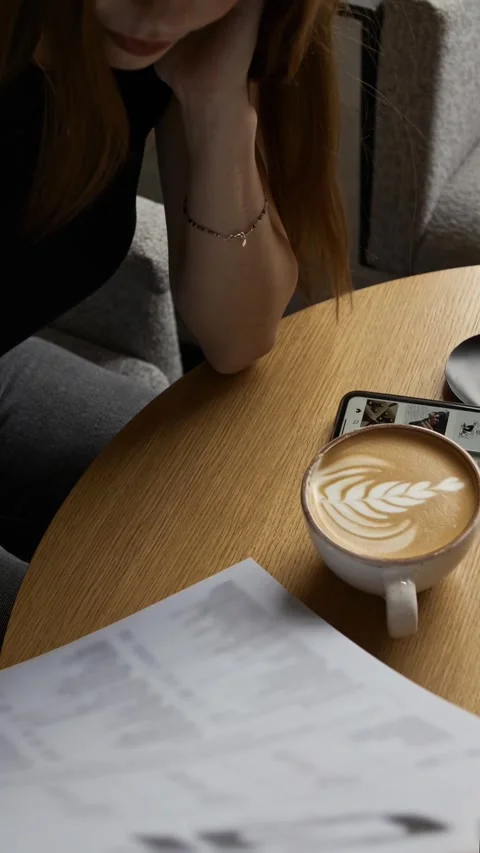 Girl studying bar menu while sitting at table in coffee shop with cup of coffee Stock Footage 310500362