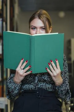 Girl is studying a book next to the rows of bookshelves. Stock Photos