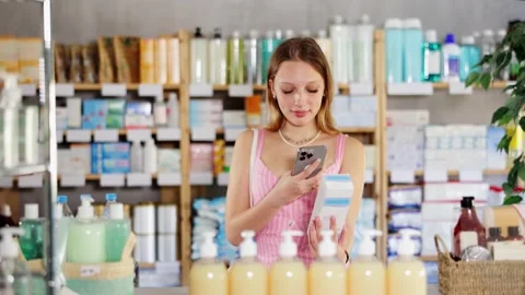 Girl in summer clothes scans code on package of cream to check the expiration Stock Footage 342125980