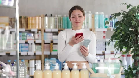 Girl in summer clothes scans code on package of cream to check the expiration Stock Footage 343709167