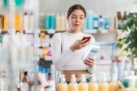 Girl in summer clothes scans code on package of cream to check expiration date Stockfoto's