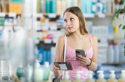 Girl in summer clothes scans code on cosmetics to check expiration date Stock-Fotos